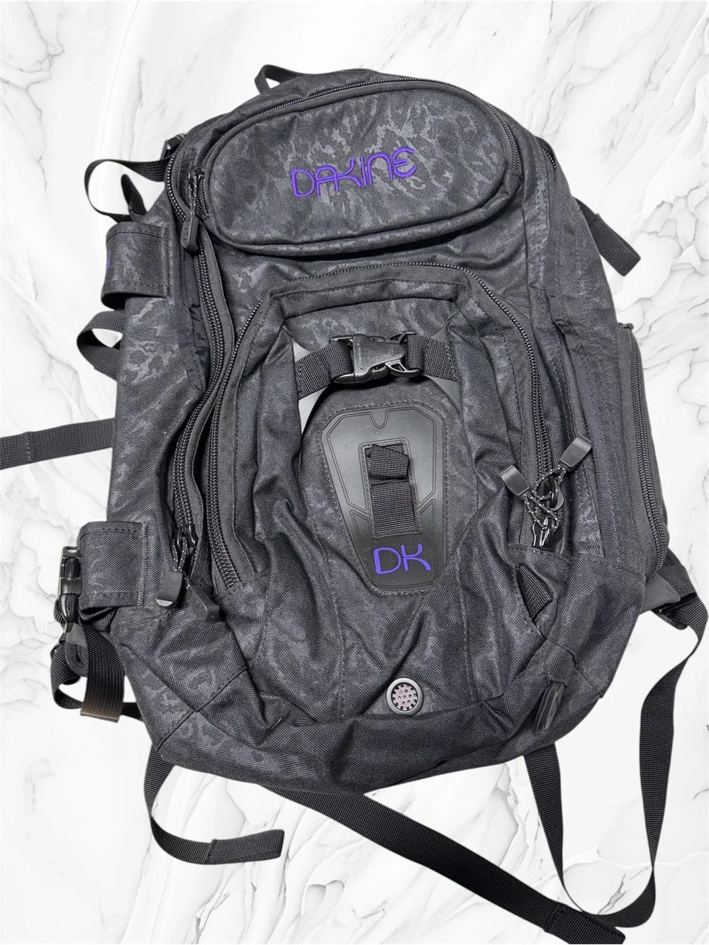 Dakine Heli Pro backpack features a black camouflage pattern and purple brandin